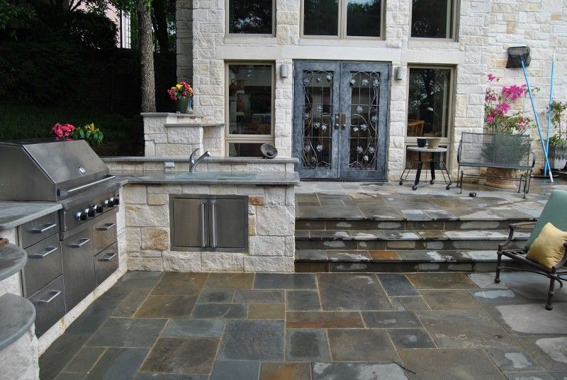 A patio with a grill and stairs leading to a house