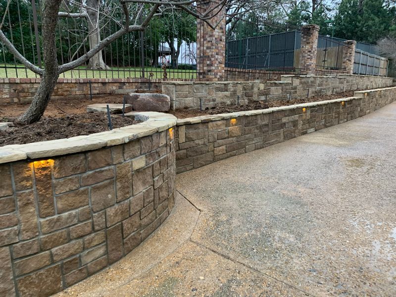 A stone wall along a driveway with lights on it.