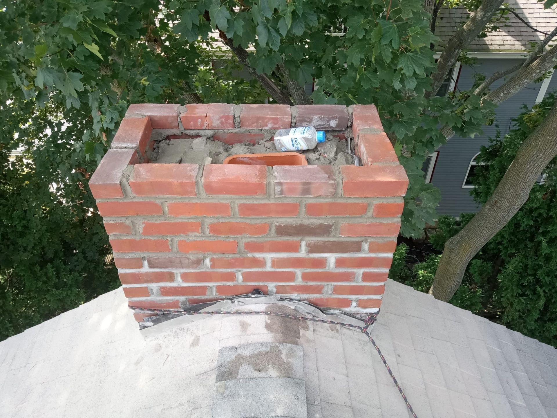 Red brick chimney on a shingled roof with a discarded plastic bottle inside the top opening.