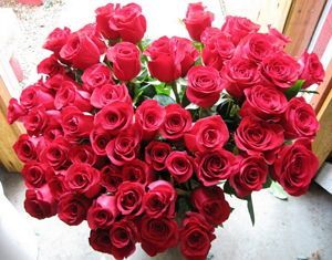 A large bouquet of red roses is sitting in front of a window.