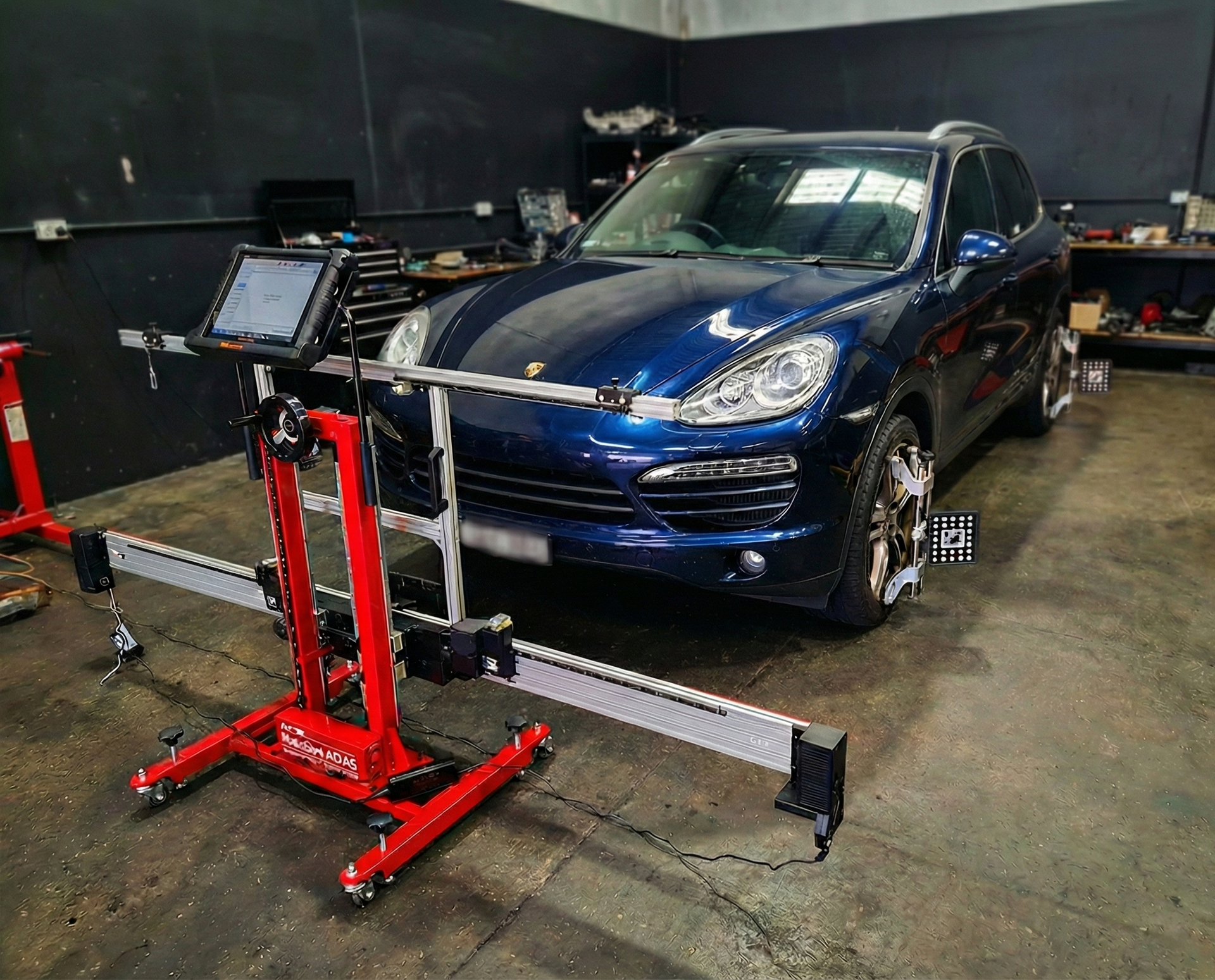 Blue SUV on a wheel alignment rack in an auto repair shop, with red alignment equipment in the foreground