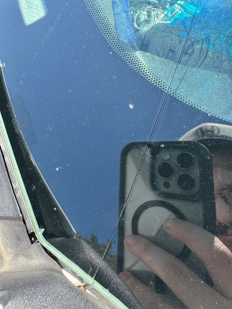 Cracked car windshield with a phone reflected in the glass and blue sky beyond