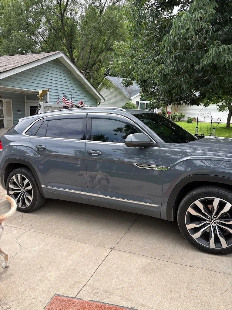 Gray SUV parked in a driveway beside a house under a leafy tree