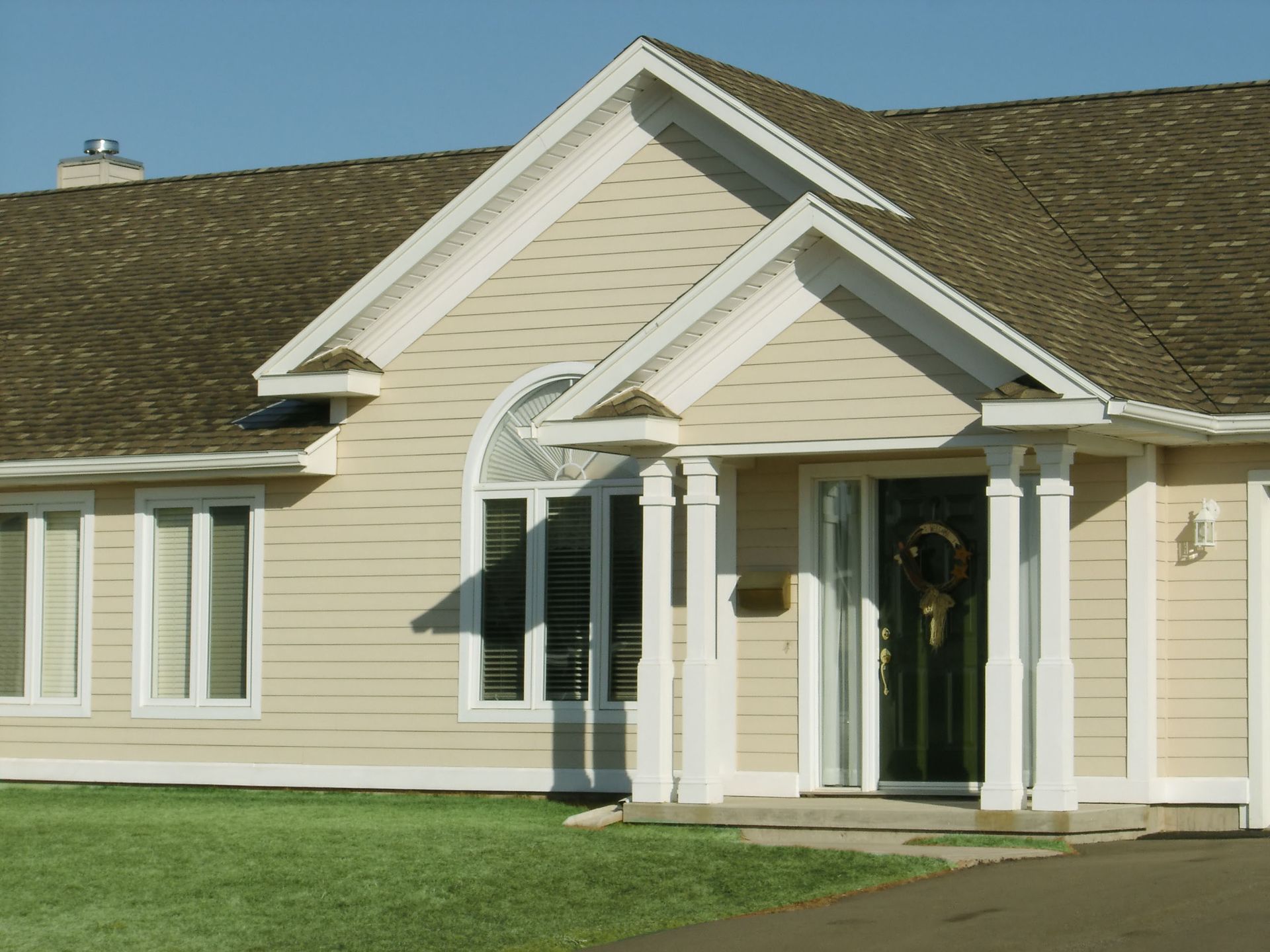 Beige house with a dark roof and green lawn. A front door is under a small portico.