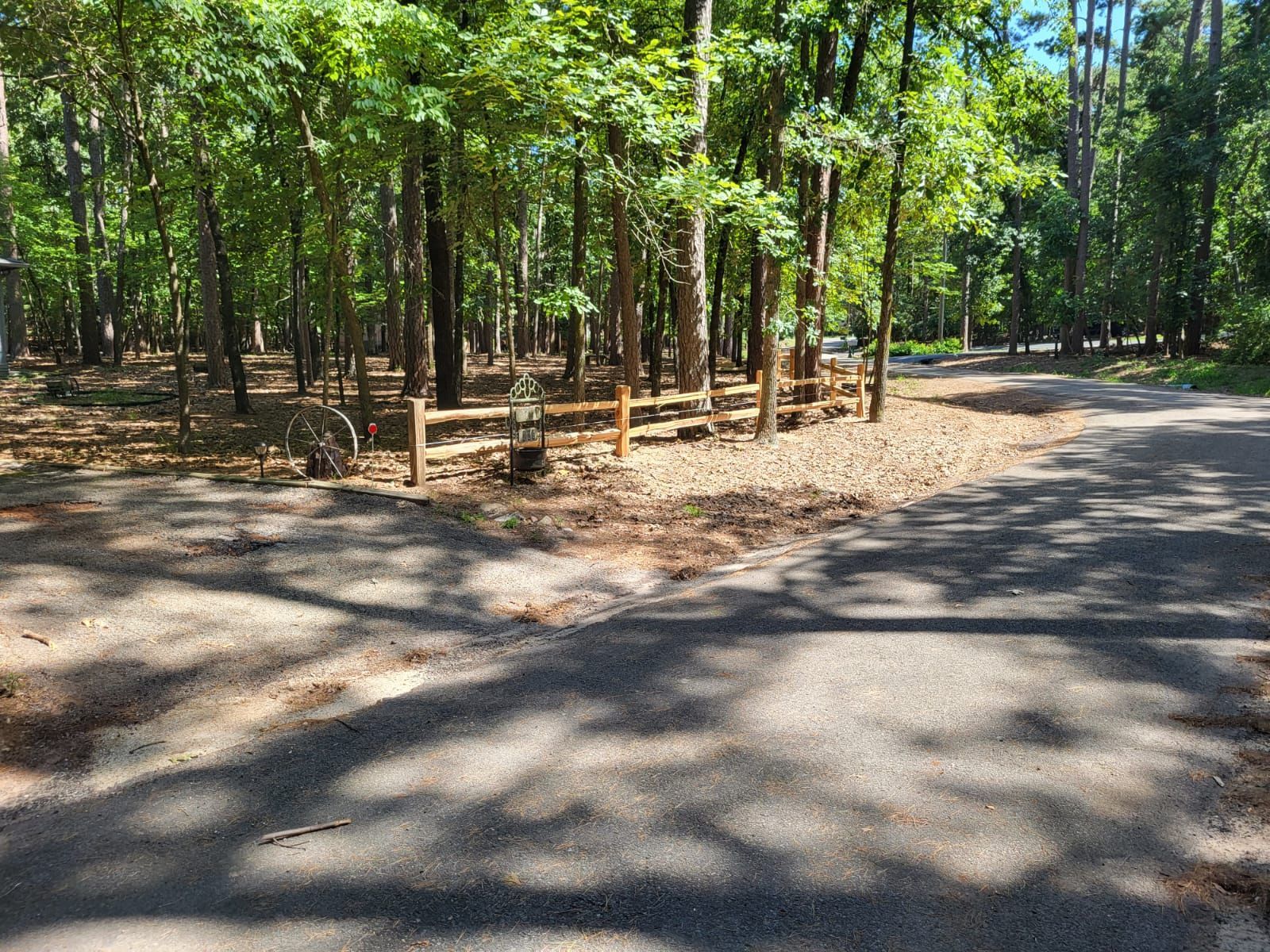A dirt road going through a forest with a wooden fence.