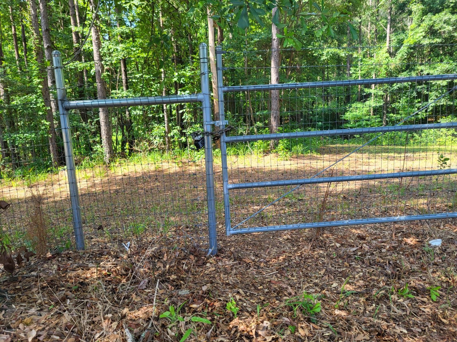 A metal gate is sitting in the middle of a field surrounded by trees.