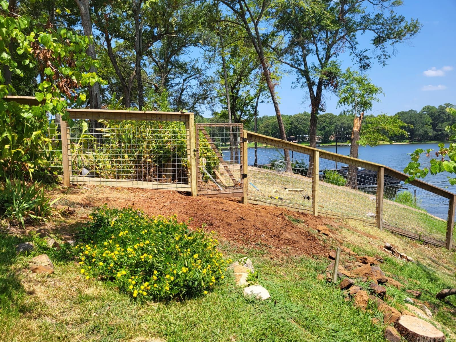 A wooden fence surrounds a yard next to a lake.