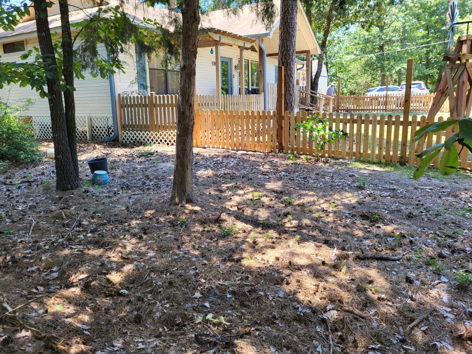 A backyard with a wooden fence and a house in the background.
