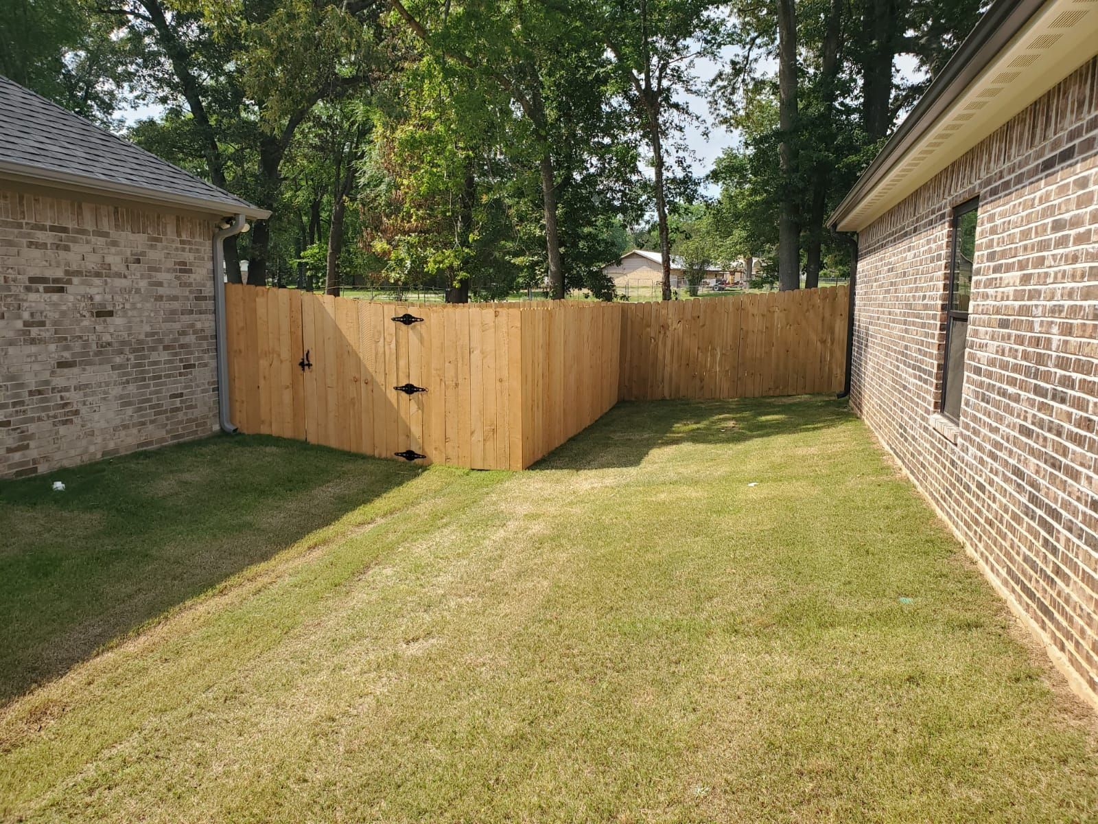 A wooden fence is in the backyard of a brick house.