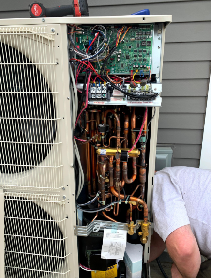 Open side of HVAC unit with copper pipes and wiring; person inspecting.