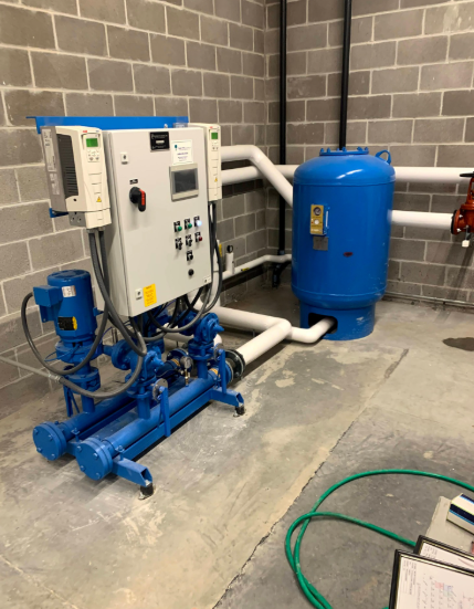 Blue water pump system with control panel and pressure tank in a room with cinder block walls.