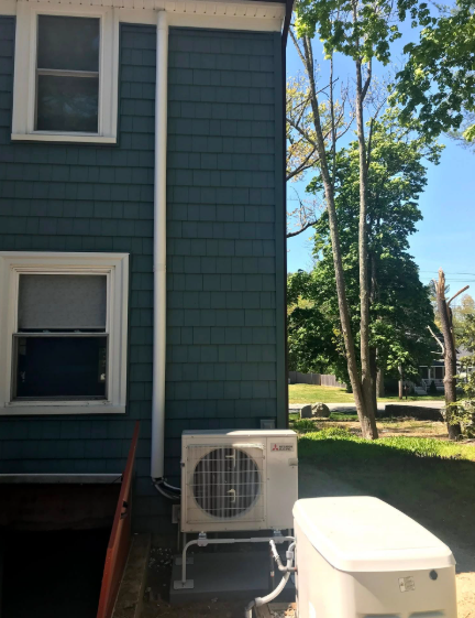 Exterior of a house with teal siding and white trim. Air conditioning unit and utility box on the ground.