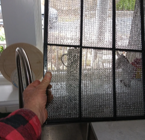 A person holding a metal mesh air filter over a kitchen sink. The filter is wet and dirty.