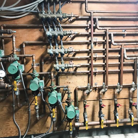 Copper pipes and valves against a wooden wall; part of a heating system.