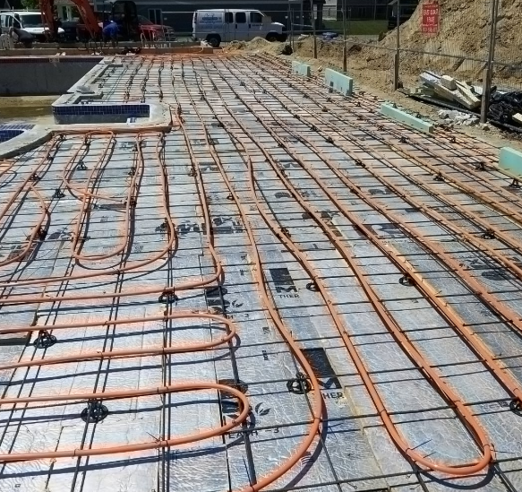 Orange tubing laid on a grid, likely for radiant heating, at a construction site.