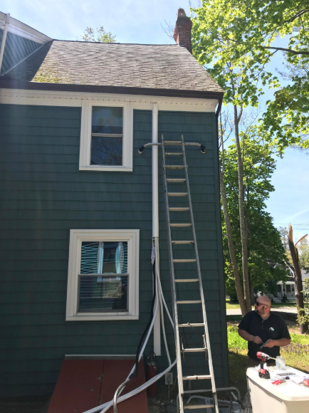 A ladder leans against a teal house. A person uses a tool nearby.