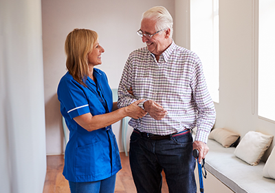A nurse is helping an elderly man walk with a cane.