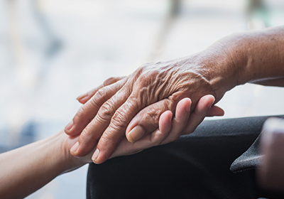 An elderly woman is holding the hand of a younger woman.