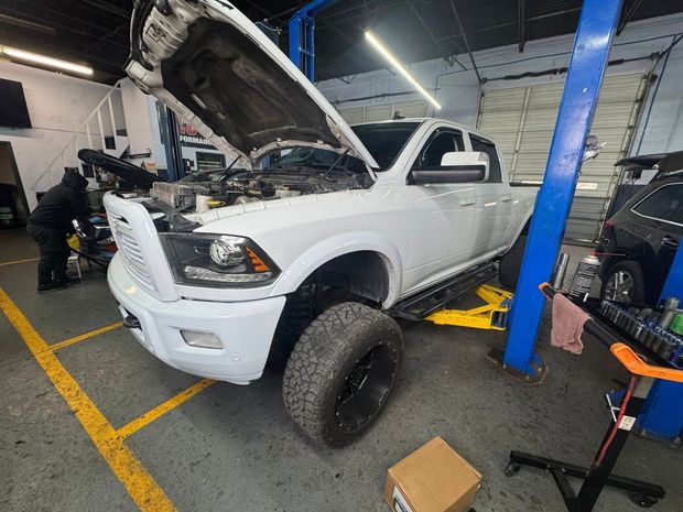 White pickup truck with hood open in a garage, raised on a lift for repair