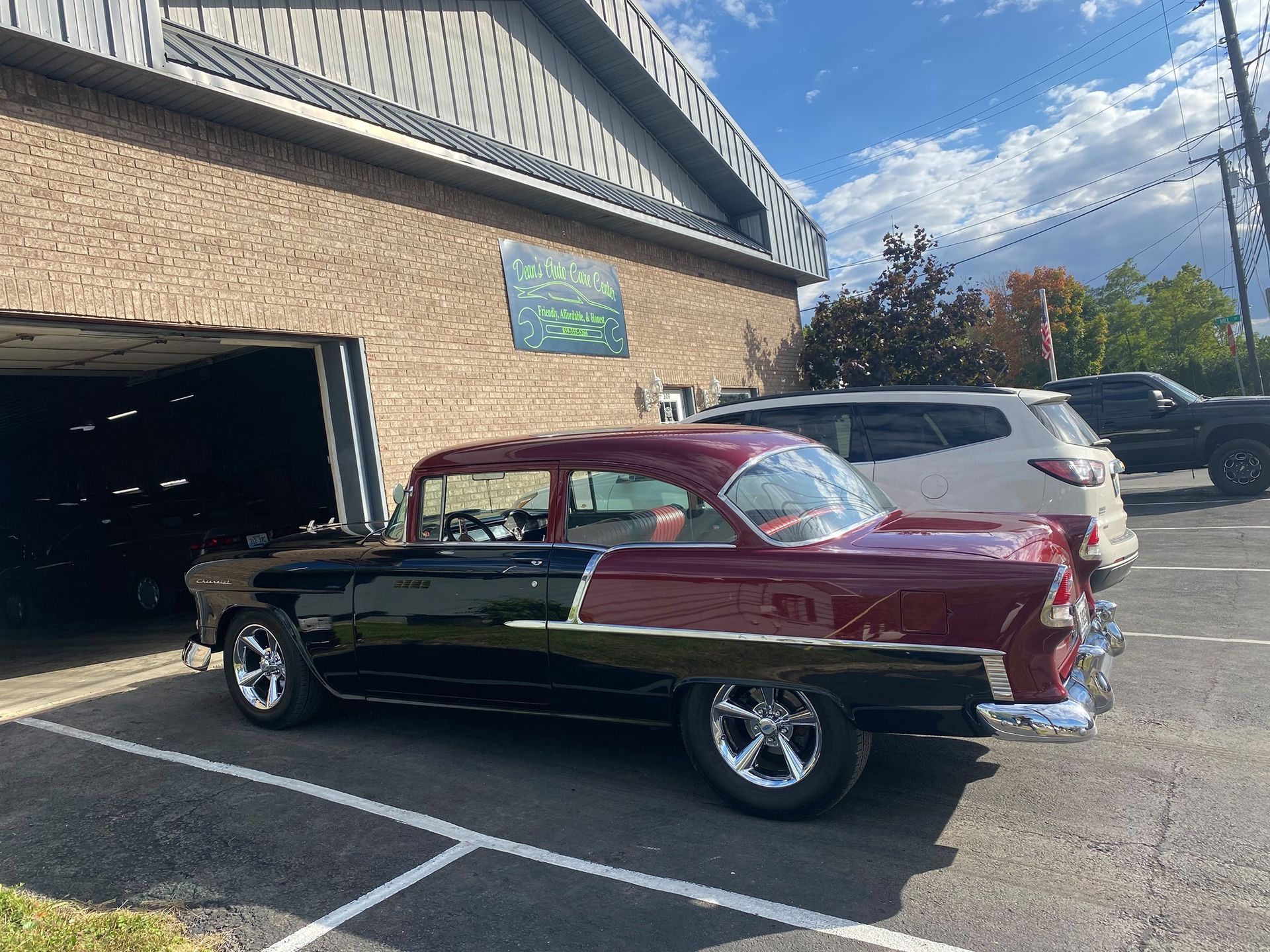 Classic red-and-black convertible parked outside a brick building beside a white SUV.