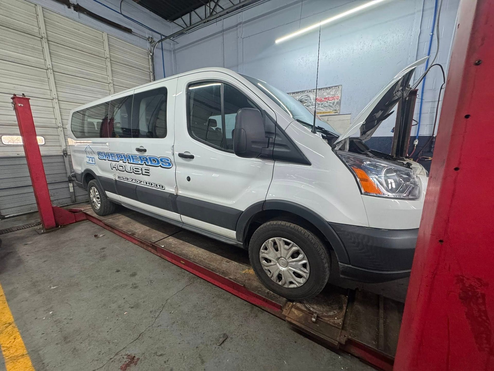 White service van on a car lift inside an auto repair shop.