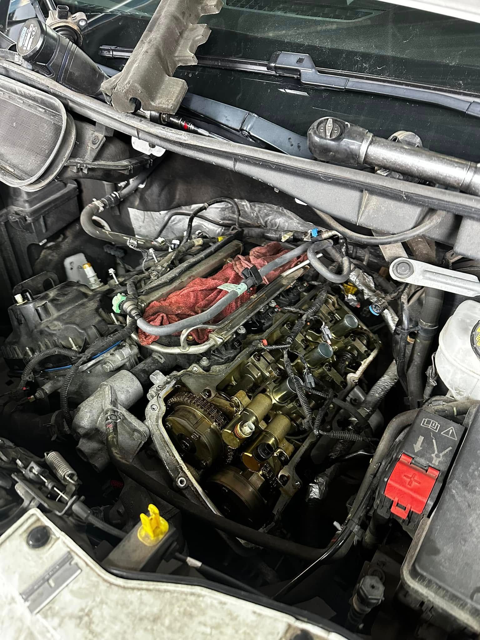 Car engine bay with top removed, exposing internal components and red wiring harness.