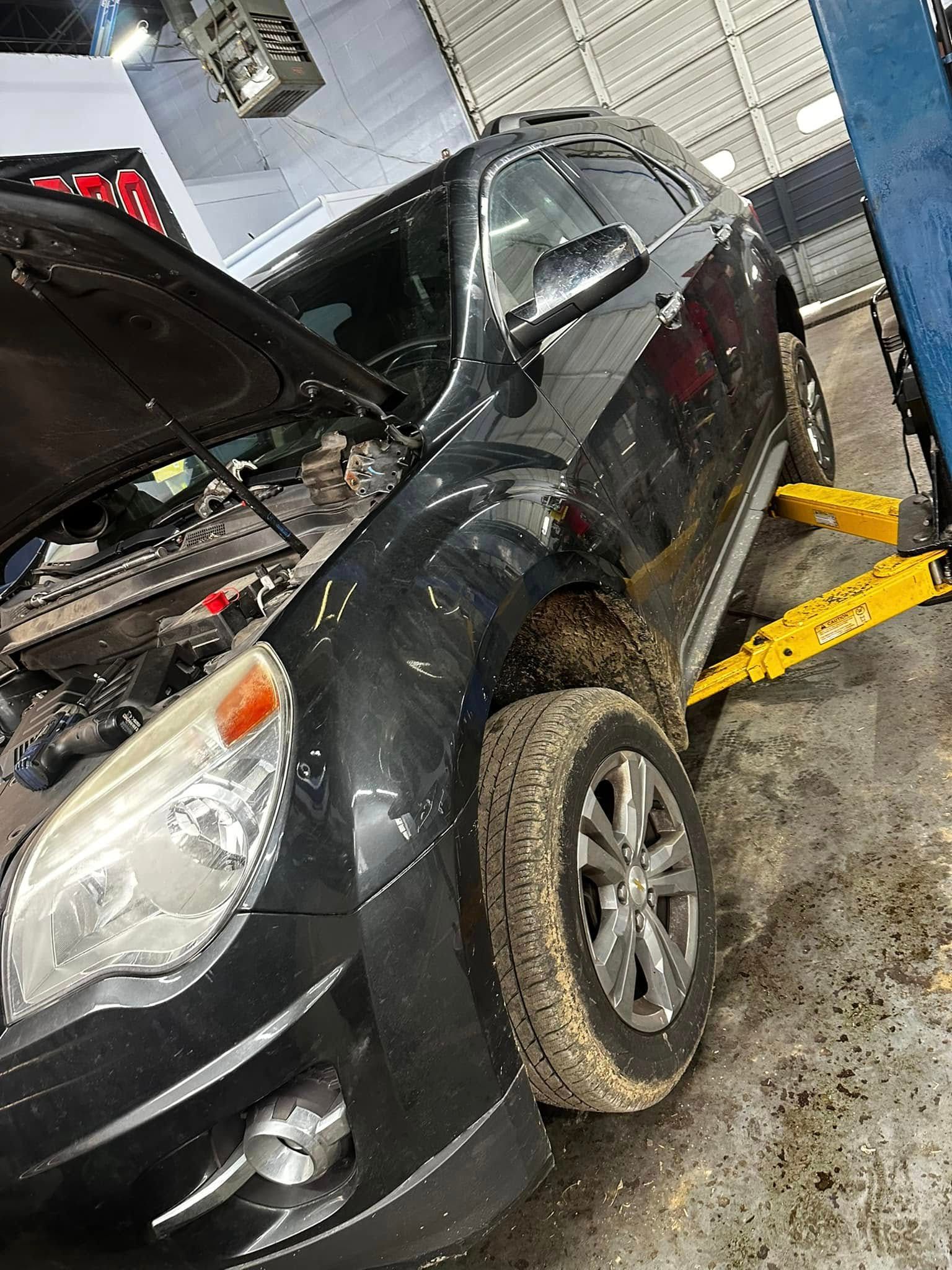 Black sedan lifted on a yellow car jack in an auto repair garage, hood open and front tire removed