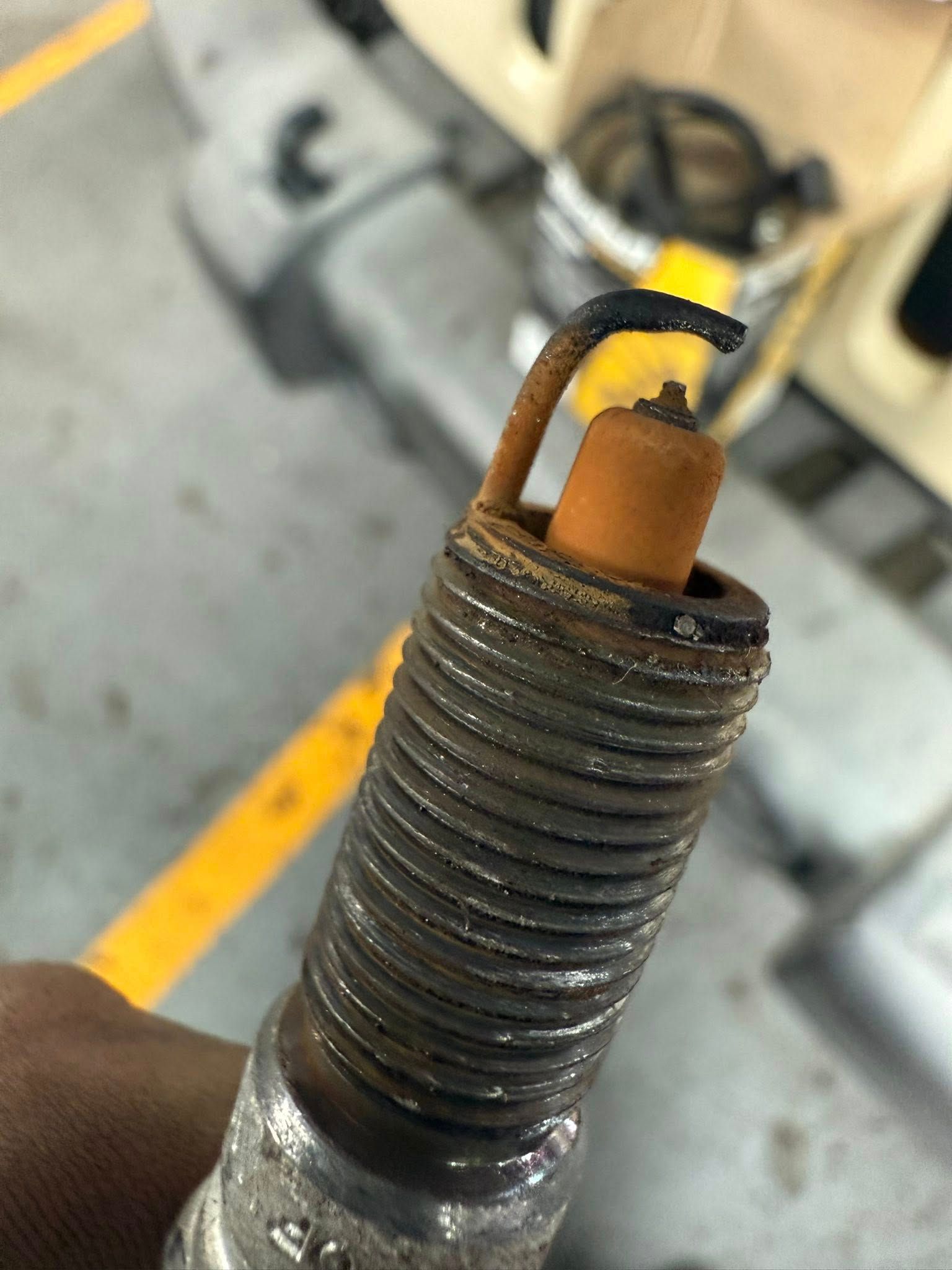 Close-up of a dirty spark plug with a blackened tip and threaded metal body in a workshop