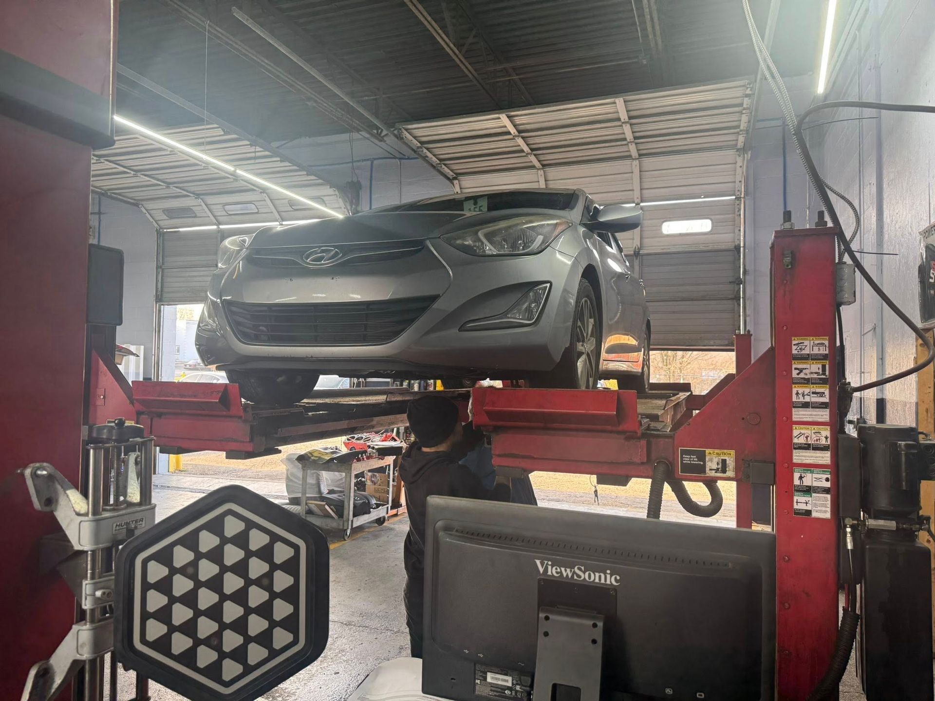Silver car lifted on a red hydraulic lift inside an auto repair shop.