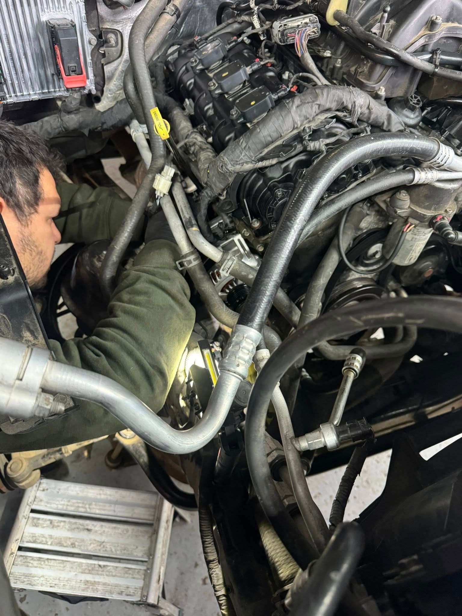 Mechanic working inside a vehicle engine bay with hoses and cables