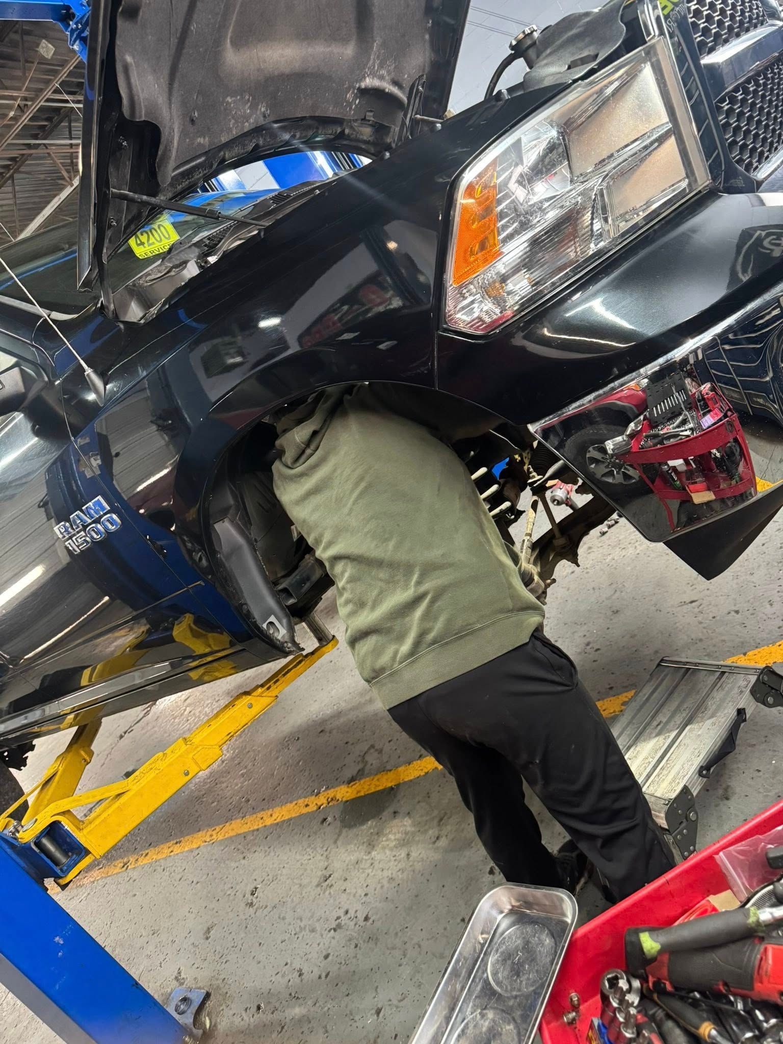 Mechanic working under a black vehicle on a lift in an auto repair shop