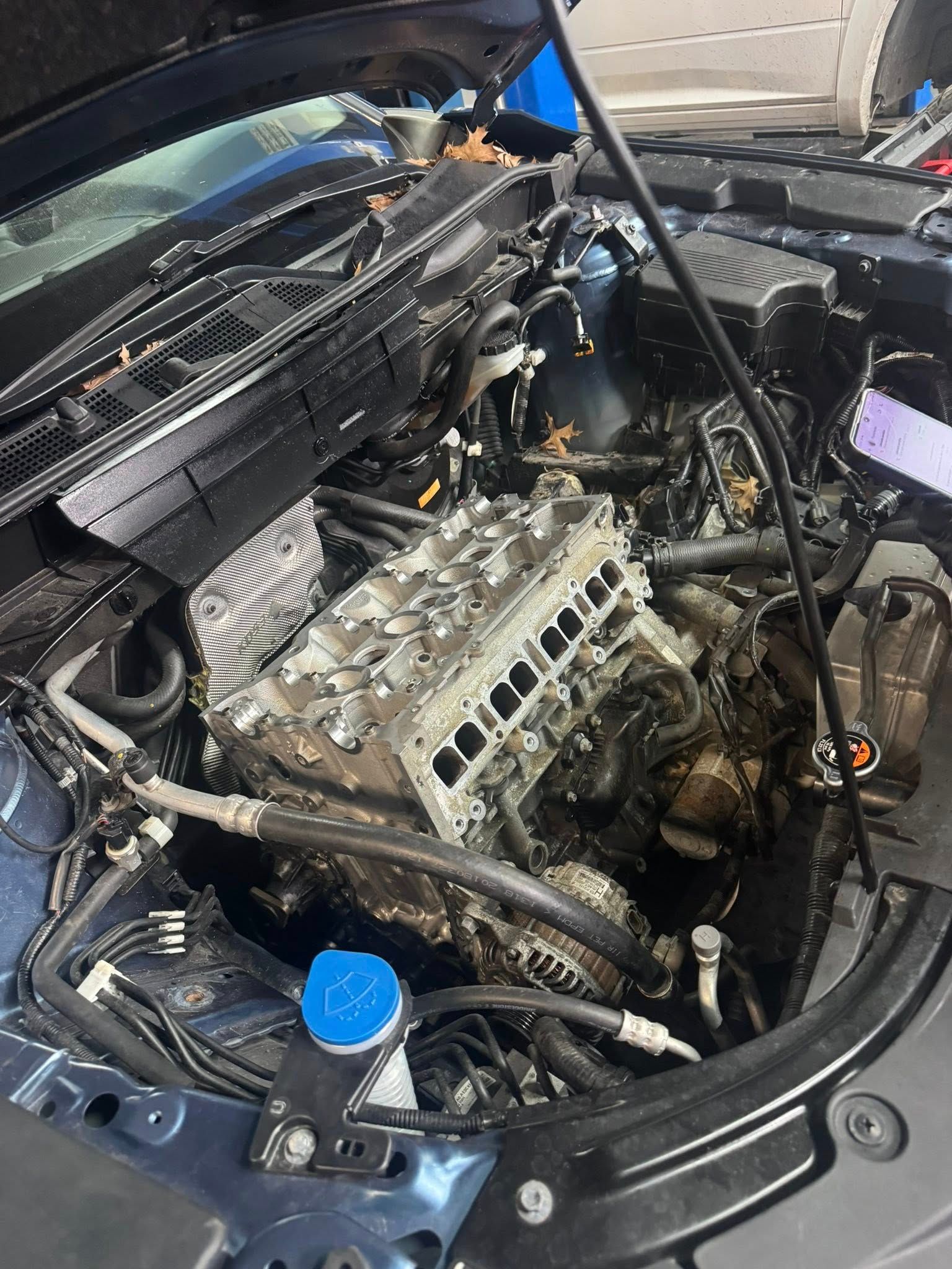 Car engine bay with a partially disassembled engine and blue fluid cap in the foreground