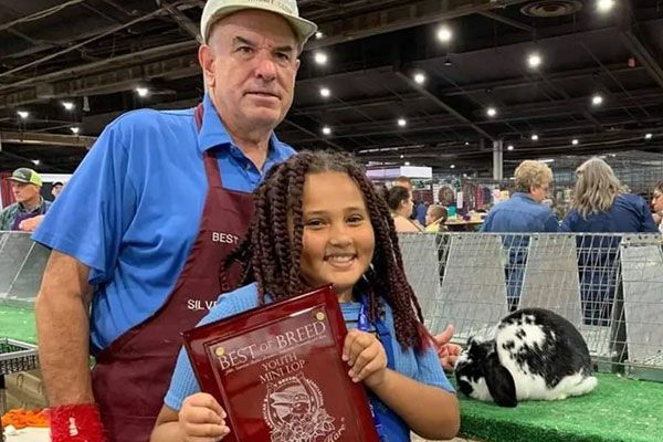 A young girl is holding a trophy in front of a table full of trophies.