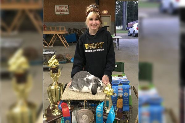 A young girl is holding a trophy in front of a table full of trophies.