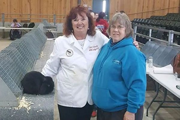 Two women are posing for a picture with a black rabbit in the background.