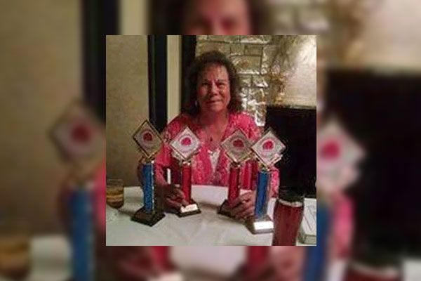 A woman is sitting at a table holding three trophies.