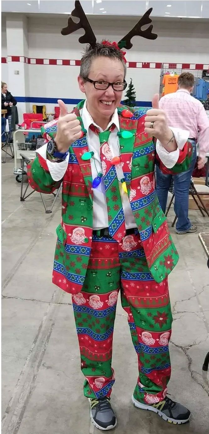 A man is wearing a christmas sweater suit and reindeer antlers.