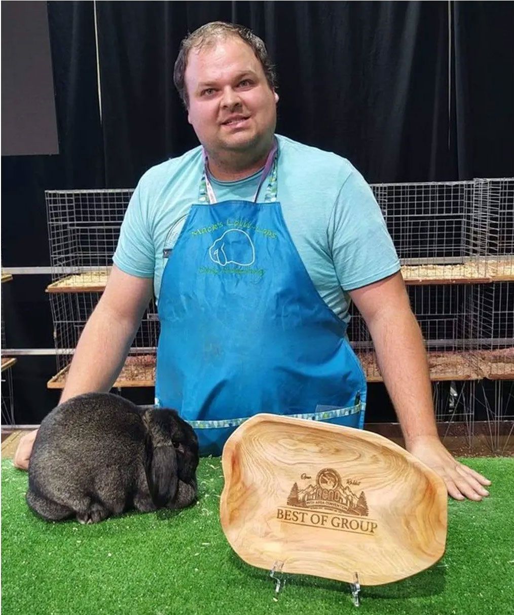 A man in an apron is standing next to a rabbit and a wooden plaque