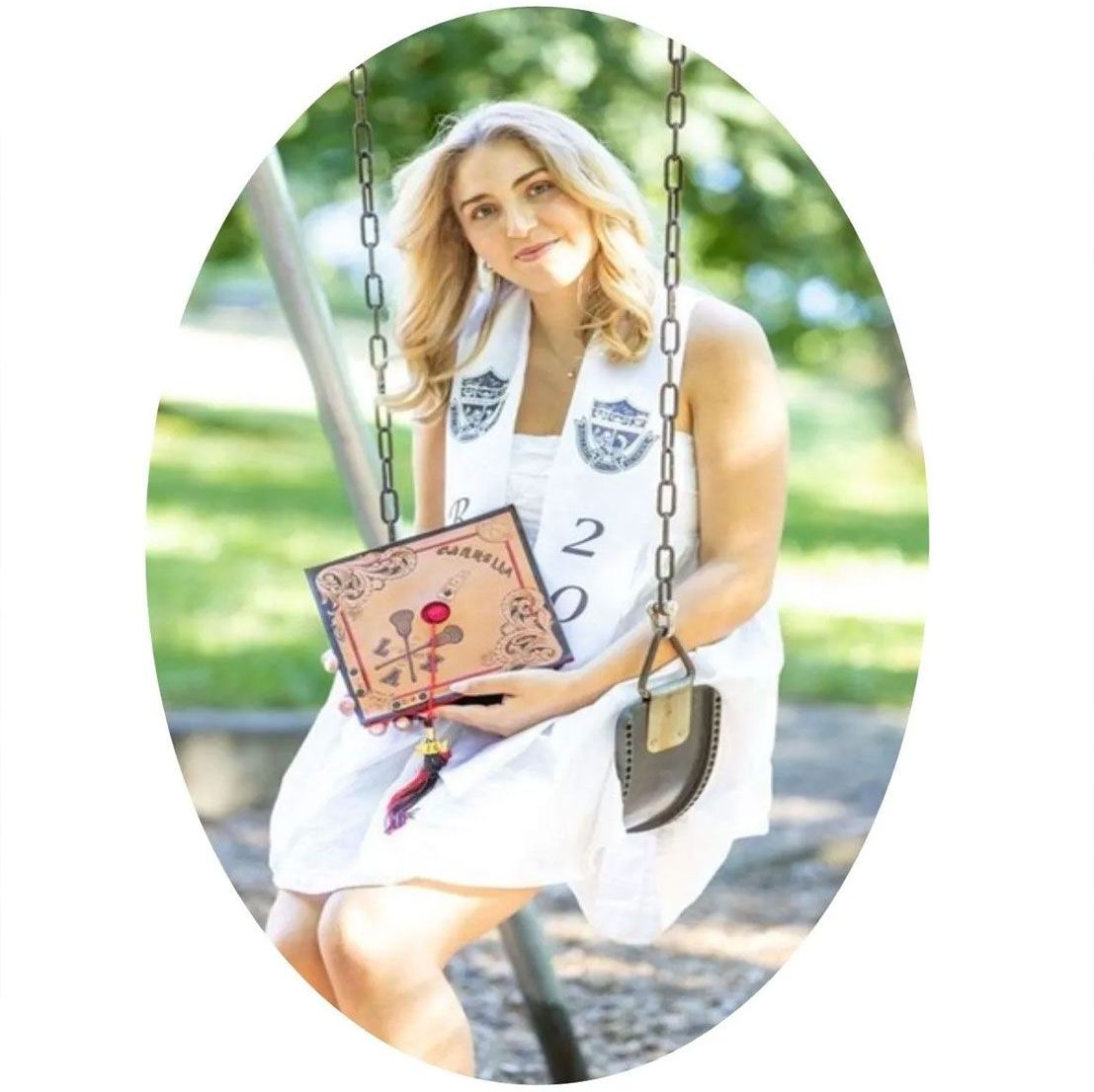 A woman in a white dress is sitting on a swing holding a book