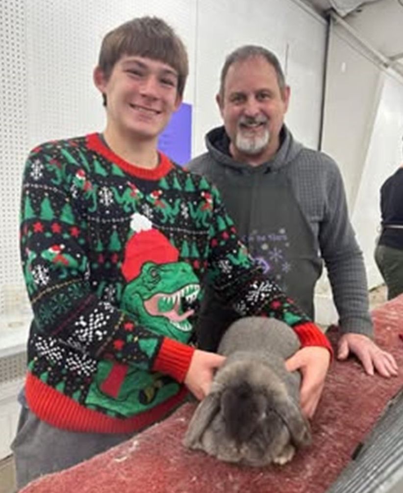 a young person and adult holding a gray rabbit, both smiling