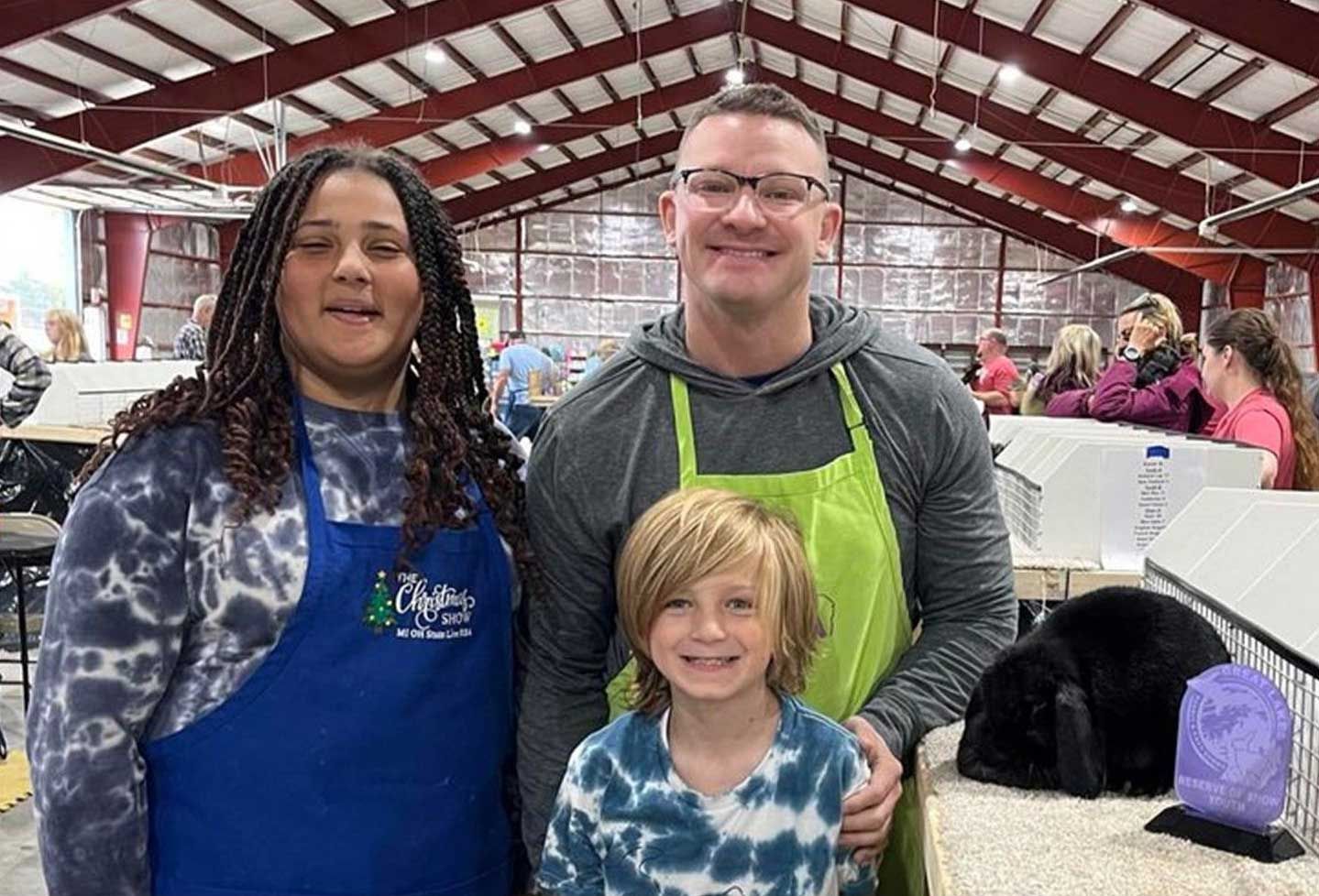 three people smiling in an event space, wearing aprons