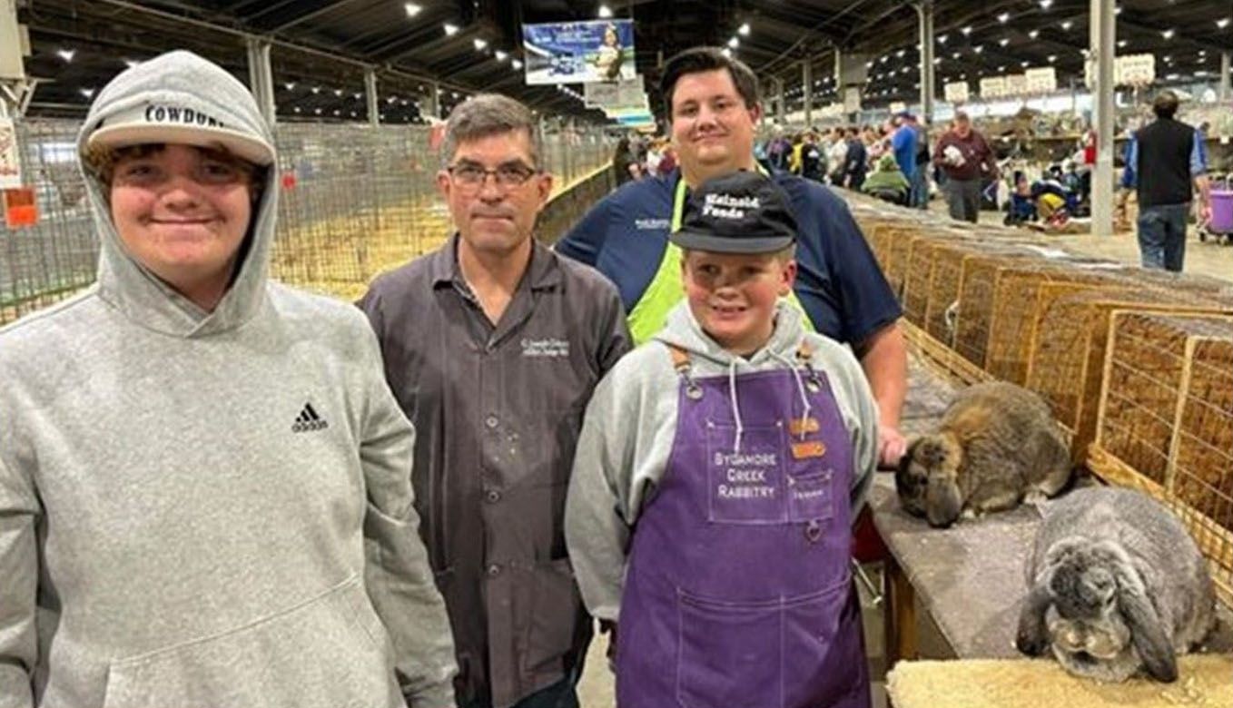 four people and two rabbits at an animal show, people stand in front of rabbit cages