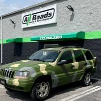 A green camouflage jeep is parked in front of a building.
