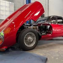 A red sports car with its hood up is parked in a garage.