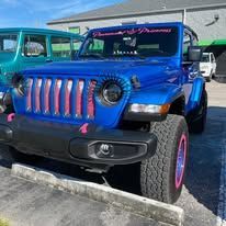 A blue jeep is parked in a parking lot in front of a building.