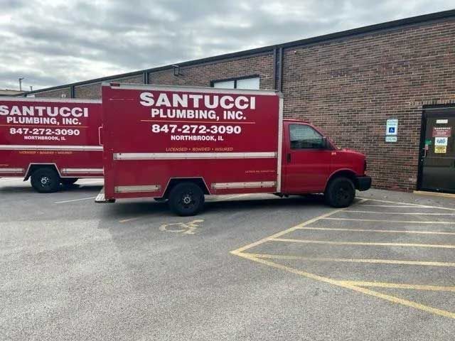 Two red vans from santucci plumbing inc. are parked in a parking lot