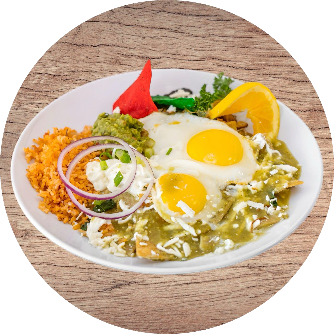 Chilaquiles with eggs, rice, guacamole, and sour cream on a white plate, topped with orange slice and tortilla chips.