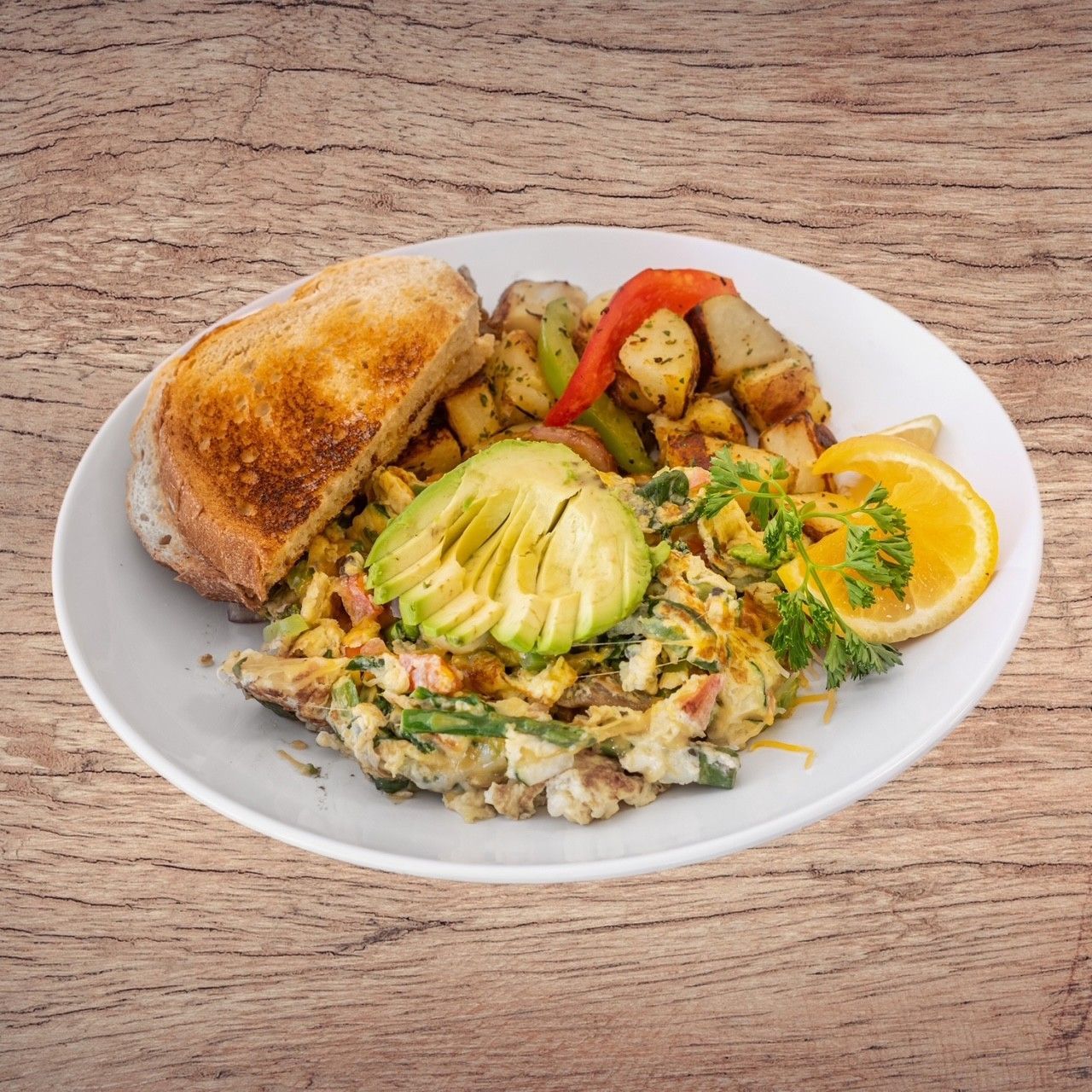 Breakfast plate with scrambled eggs, avocado, potatoes, toast, and an orange slice.