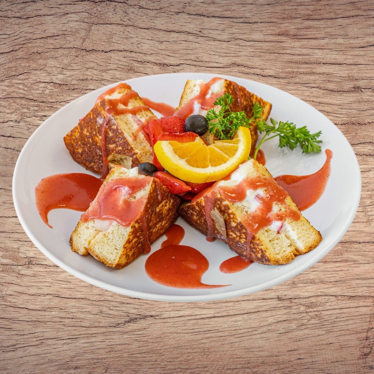 French toast with fruit and sauce on a white plate, wood background.