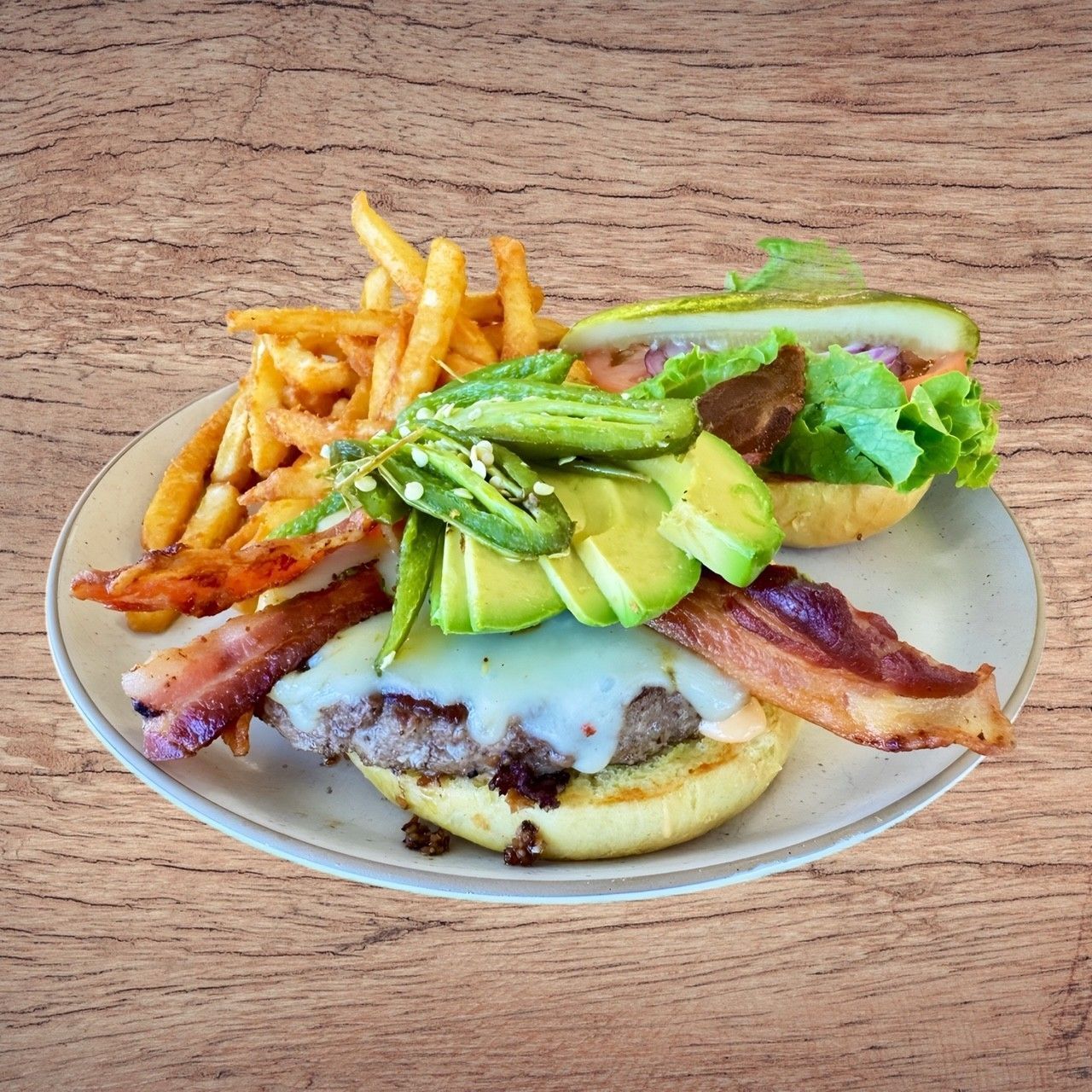Burger with bacon, avocado, lettuce, and fries on a plate against a wooden background.
